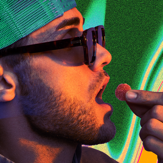 Man wearing glasses and a green cap holding a round candy near his open mouth, against a colorful background.