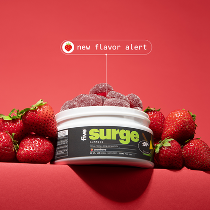 Tub of Five Surge GUMMIES (strawberry) with sugar-coated gummies and fresh strawberries; label shows "new flavor alert".