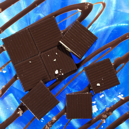 Dark chocolate squares with ridged tops, sea salt flakes and chocolate drizzle on shimmering blue background