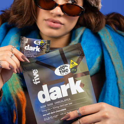 Person holding dark sea salt dark chocolate bag labeled five, 100MG THC PER BAG, 10mg thc + 50mg cbd per bar, 21+