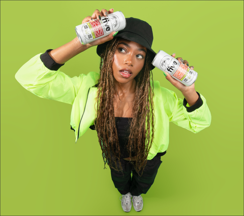 Woman in a neon green jacket and black bucket hat holding two cans of Five beverage, one labeled 'Five' with 'Zero Sugar' and 'Zero Calories' text visible.