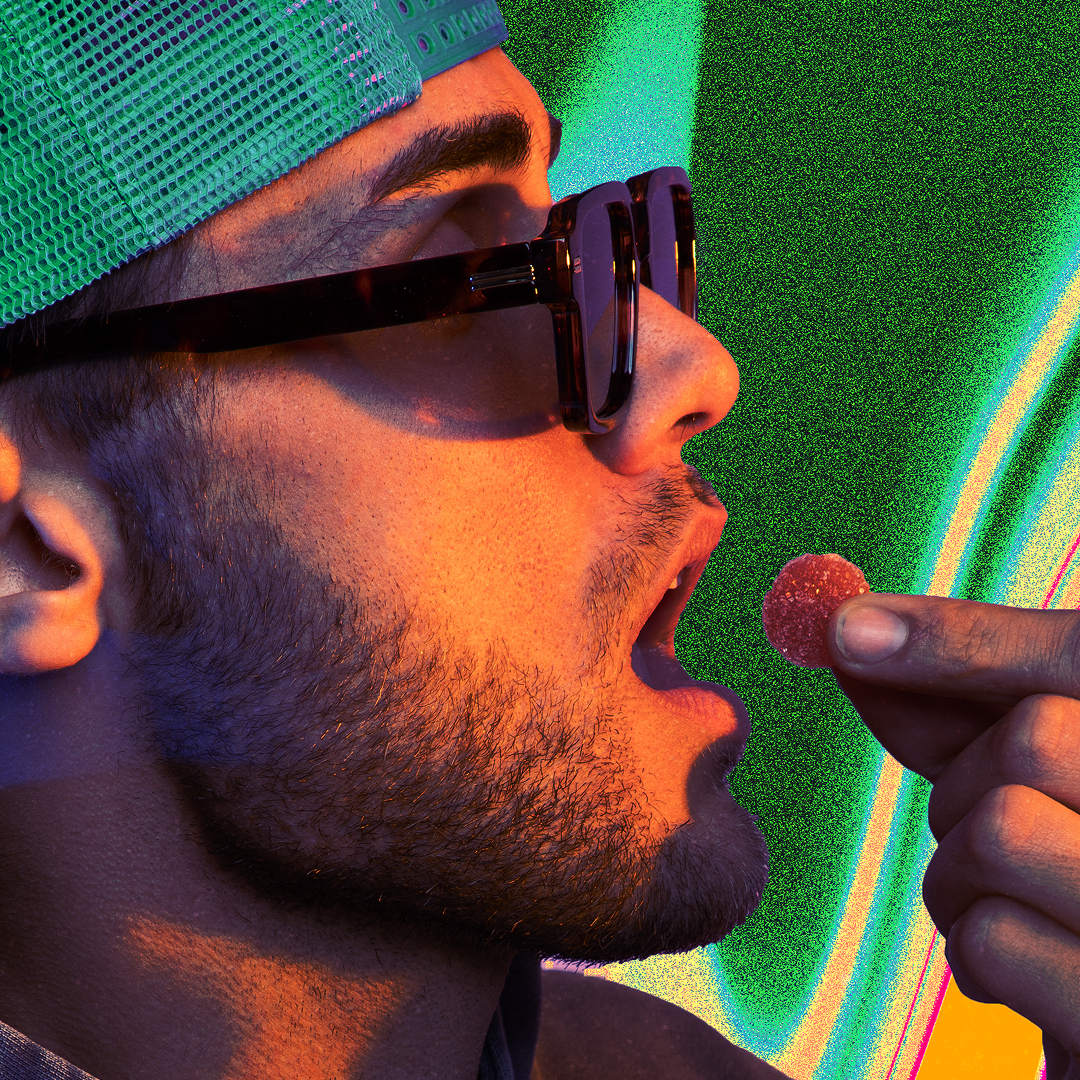 Profile of man wearing cap and sunglasses holding a sugar-coated red gummy near his open mouth